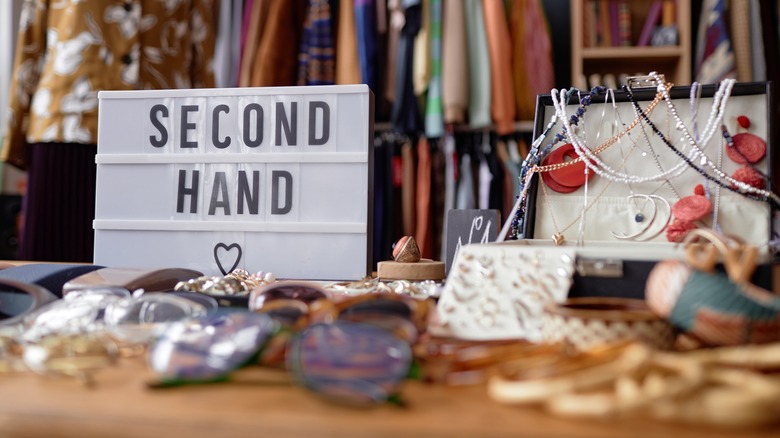 "Second hand" sign in a thrift store on a wooden table alongside accessories