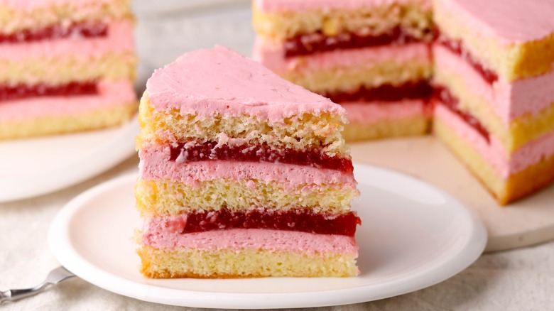 A piece of layered strawberry cake with jam on plate