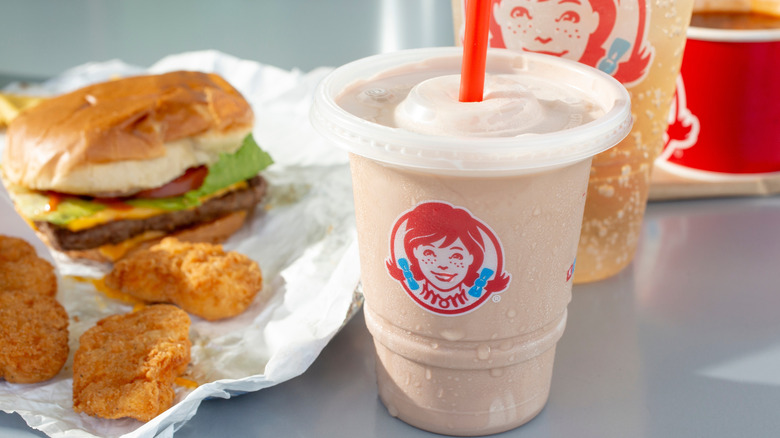 A chocolate Wendy's Frosty sits near other Wendy's food and a soda