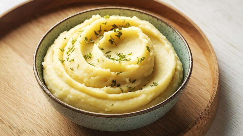 A bowl of creamy, fluffy mashed potatoes topped with herbs on a serving platter.