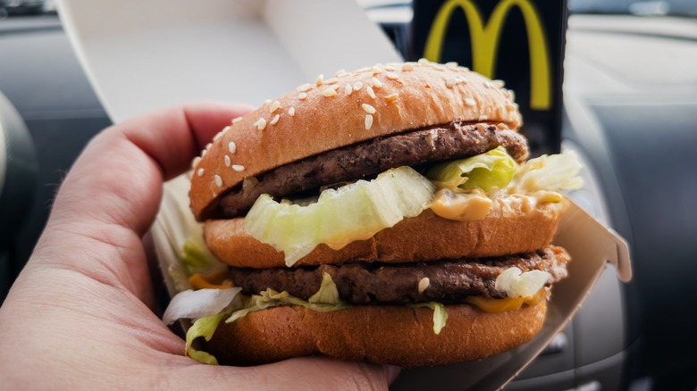 A hand holds a McDonald's Big Mac while sitting in a car