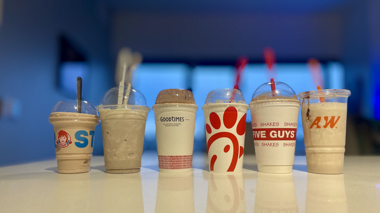 Lineup of six different fast food milkshakes on a white counter
