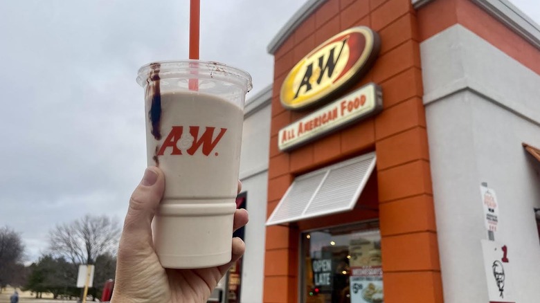 An A&W chocolate milkshake with a streak of chocolate on the cup is held up outside an A&W restaurant.
