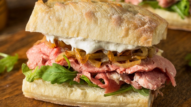 Steak sandwich on baguette with arugula, caramelized onions