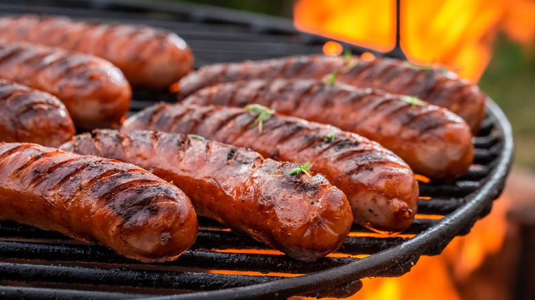 Grilled sausages sit on a barbecue under an open flame