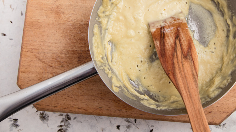 A bubbling roux in a pot with a wooden spoon sits on a board