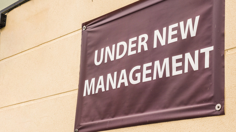 Under new management banner affixed to a stone wall
