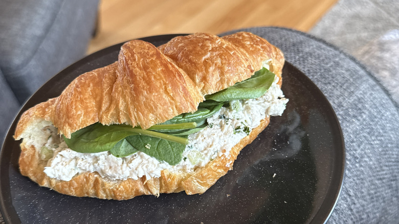 A sandwich made from chicken salad and spinach on a croissant sits on a black plate.