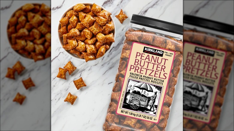 A container of Kirkland Signature Peanut Butter Pretzels sits next to a bowl of the snacks on a marble surface.