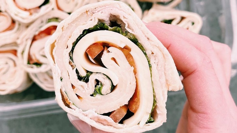 A hand holds a Kirkland Signature Roasted Chicken & Swiss Roller.