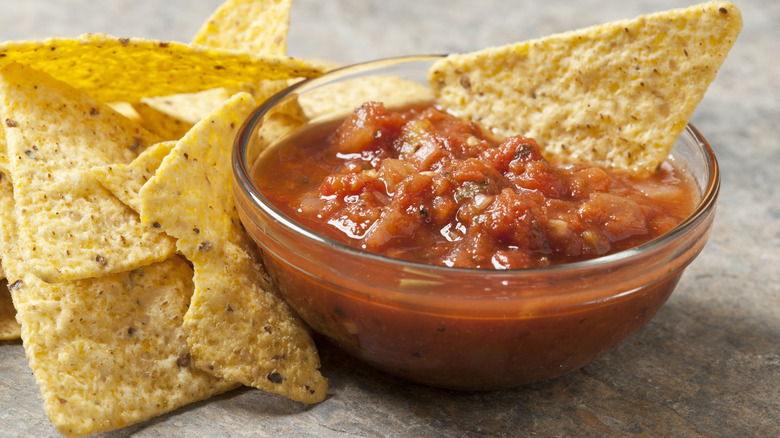 A clear, glass bowl of salsa with yellow corn tortilla chips.