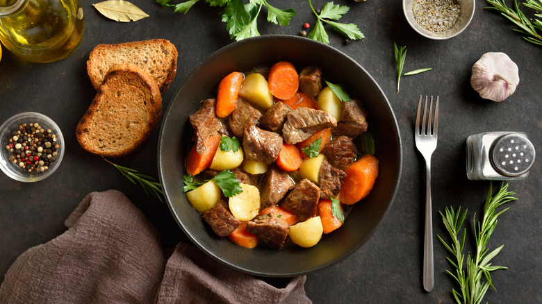 Beef stew in a black bowl with fresh herbs and two bread slices around it