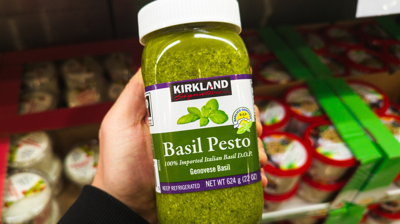 hand holding up a jar of kirkland basil pesto in Costco