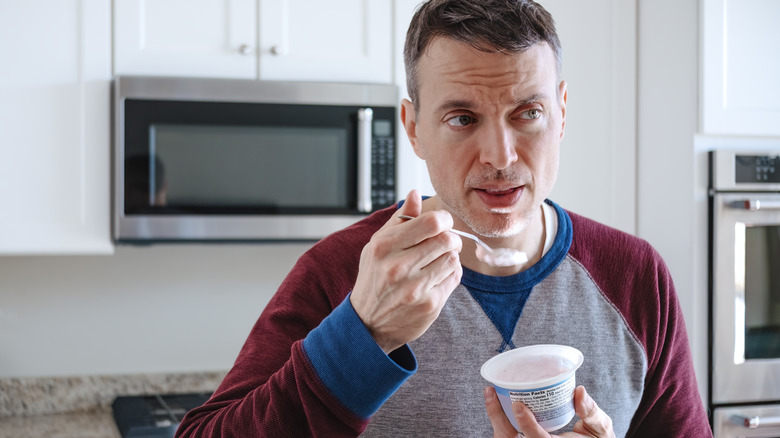 An adult man eating a cup of yogurt