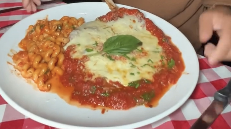 Chicken parmigiana is served alongside pasta.