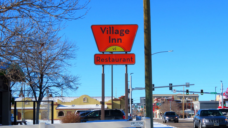 A Village Inn Restaurant sign stands next to a busy highway