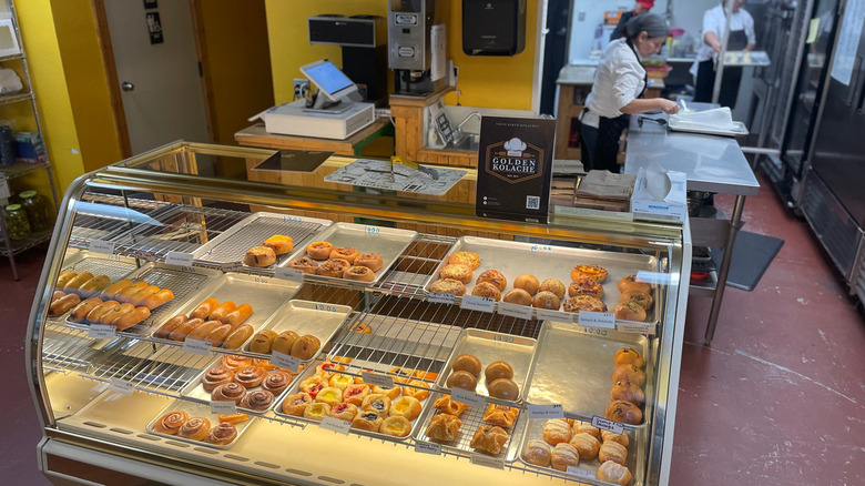 Photo of a half-empty pastry case behind which staff work on baking more treats