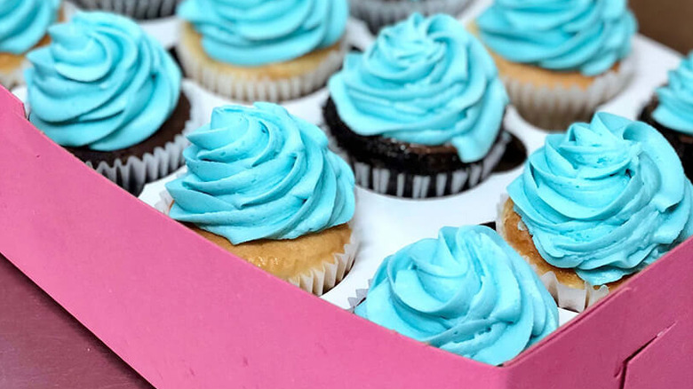 A pink pastry box filled with chocolate and vanilla cupcakes topped with sky blue frosting