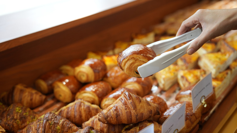 Person selecting croissant from a pastry case