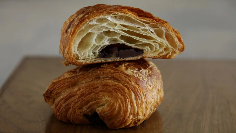 Two halves of a delicate, chocolate croissant stacked on top of each other on a dark wood table