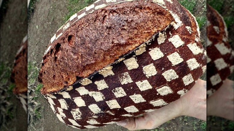 A hand holding a full loaf of 100% whole grain, "warthog" red wheat loaf from Mel the Bakery