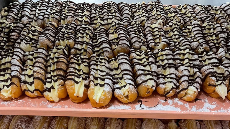 A shelf displaying 30+ "West Virginia Hot Dogs," aka eclair-shaped pastry filled with Bavarian cream and topped with powdered sugar and chocolate drizzle