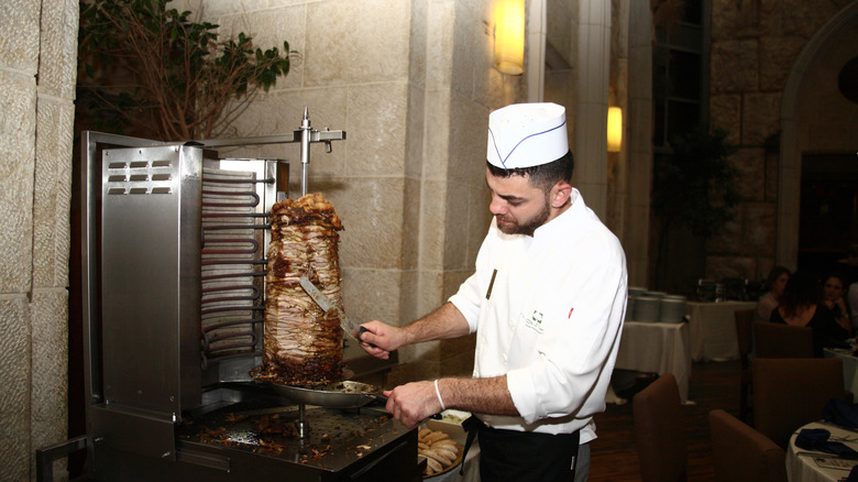 a chef slicing kebab meat from a large rotisserie