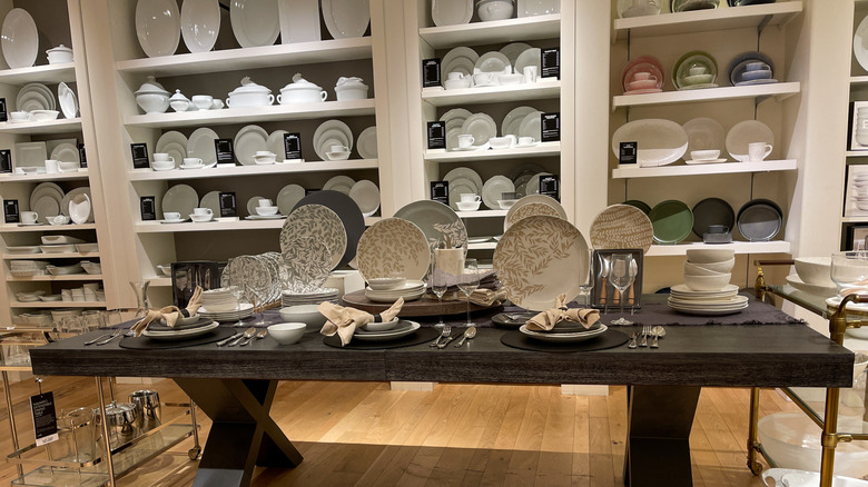 A display of plates and cutlery in front of shelves of different ceramics in a Williams Sonoma