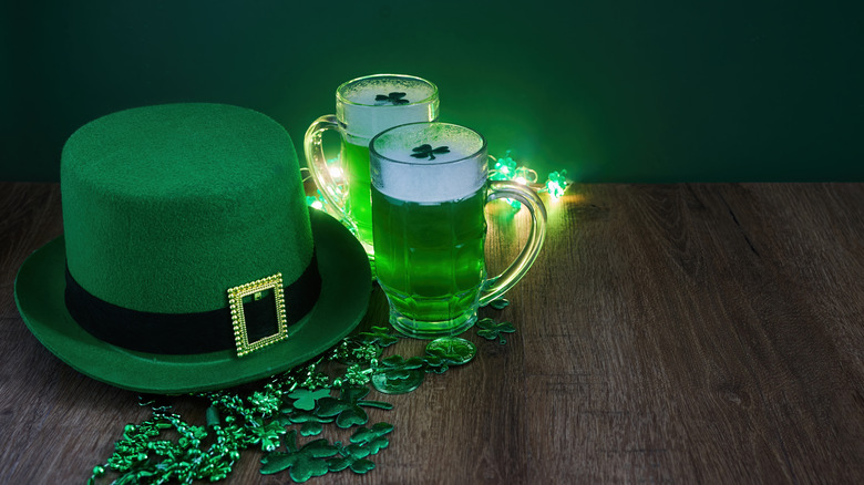 A leprechaun hat, St. Patrick's Day decorations, and two mugs of green beer sit on a table