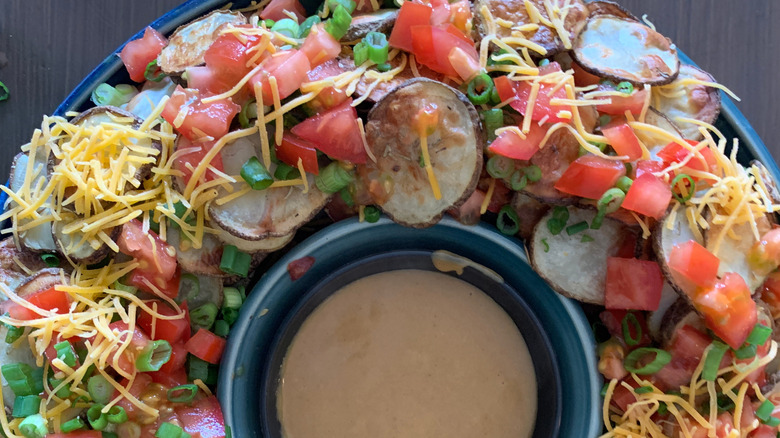 Plate of Irish nachos topped with cheese, tomatoes, and scallions with dipping sauce