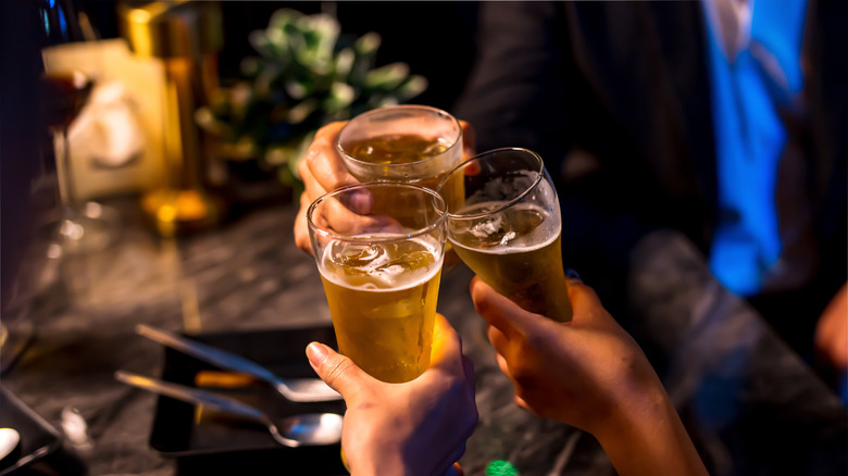 Friends toast clink glasses at a pub over a table covered with food
