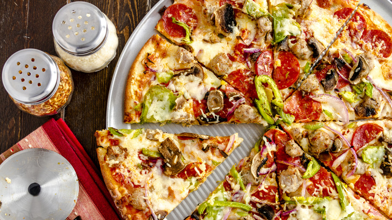 A pizza with a parmesan and red pepper flake shaker next to it.