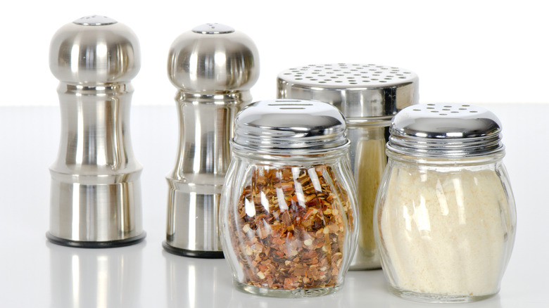 A salt and pepper shaker next to a parmesan and red pepper dispenser on a table.