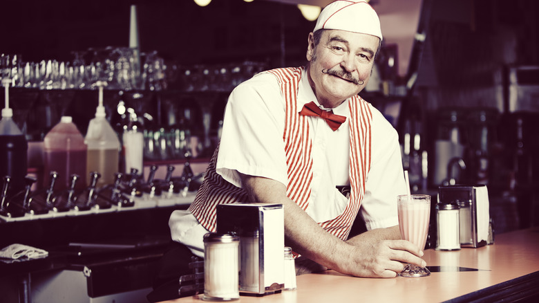 A worker in a candystripe uniform behind the counter at a soda fountain