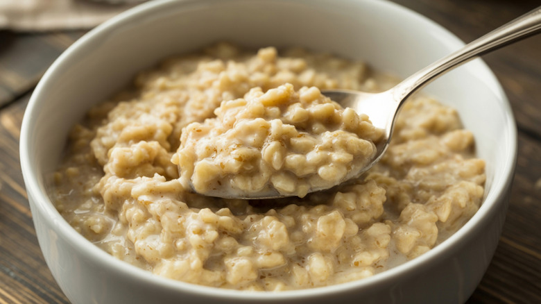 Oatmeal is scooped out of a bowl with a metal spoon.