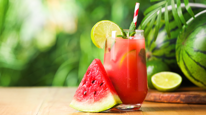 A watermelon cocktail outside on a wooden table with fresh mint and a lime wheel.