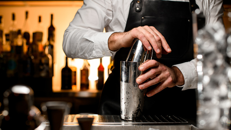 A bartender using a cocktail shaker at the bar, the bottom part of the shaker appears to be ice cold.