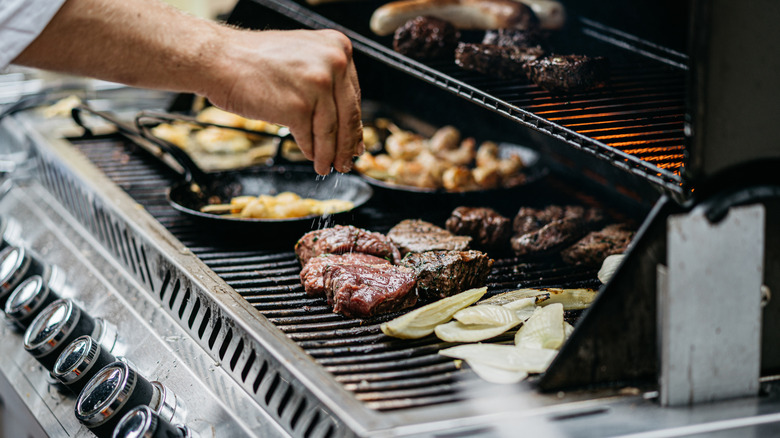 Chef adding salt to steaks on a loaded grill.