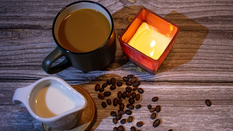 Mug of coffee next to a candle and a white container of cream
