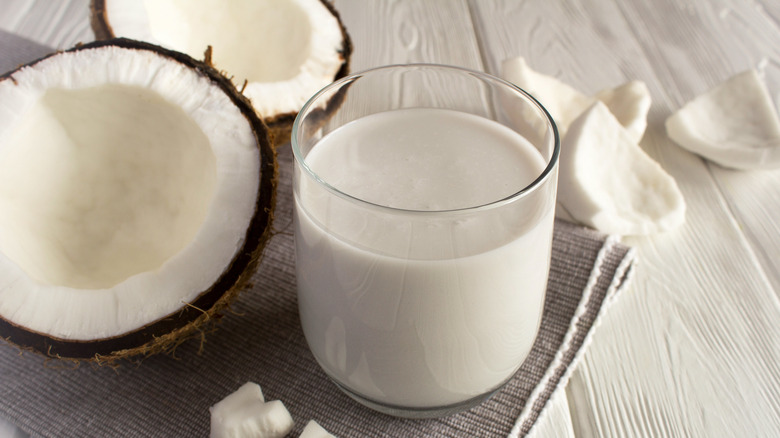Coconut milk in a glass next to 2 coconut halves and a few slices of coconut meat