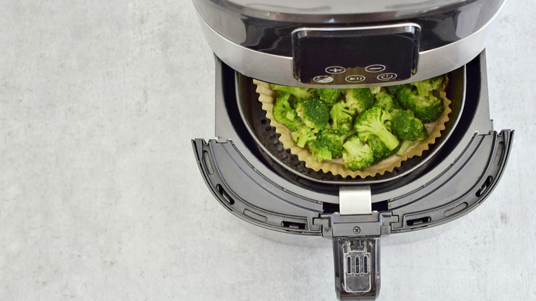 An air fryer basket is pulled out half-way, revealing broccoli inside