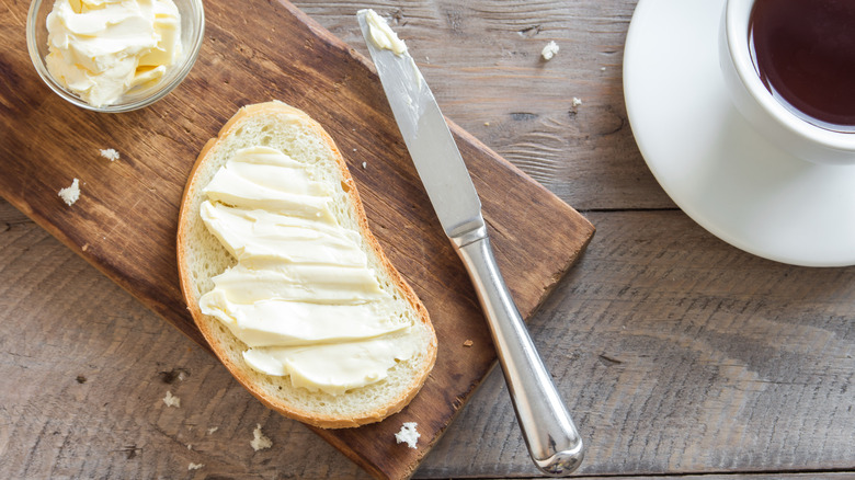 Creamy butter spread over a slice of bread on a wooden board