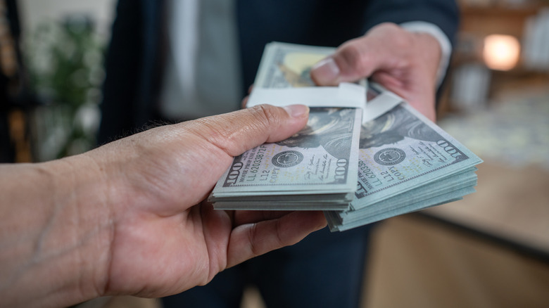 A person handing two stacks of hundred dollar bills to another person
