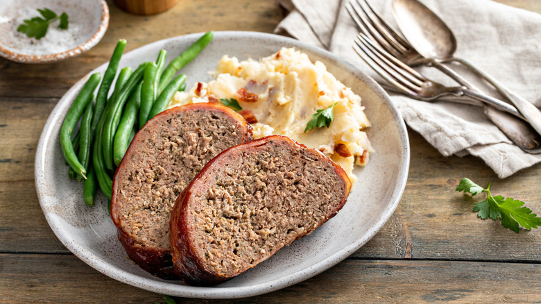 A meatloaf meal with a side of boiled green beans and mashed potatoes.