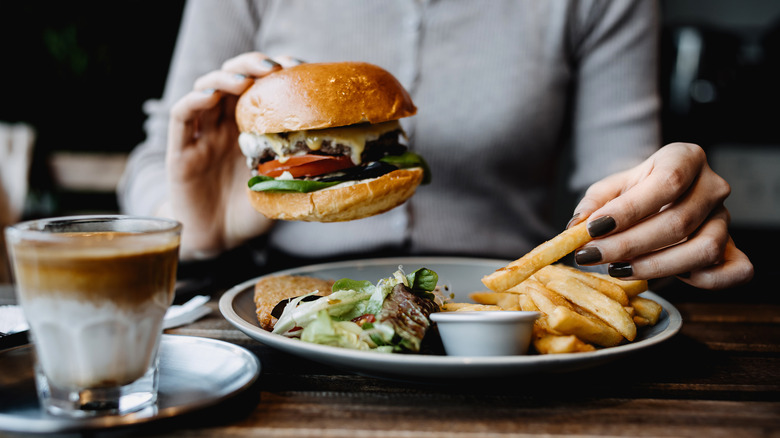 A person eats a burger with fries and a macchiato