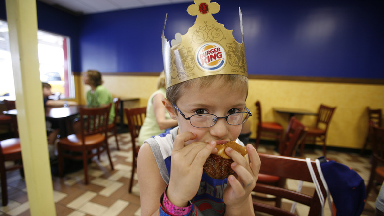 A young child wearing a Burger King crown enjoys a hamburger in a Burger King restaurant