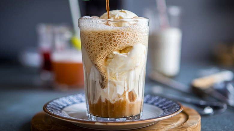 A root beer float with a thin stream of soda being poured in