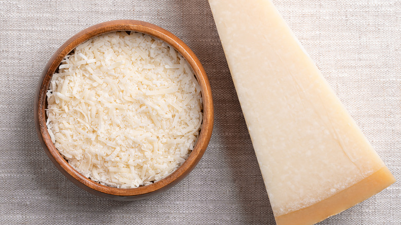 A brick of parmesan next to a bowl of grated parmesan.