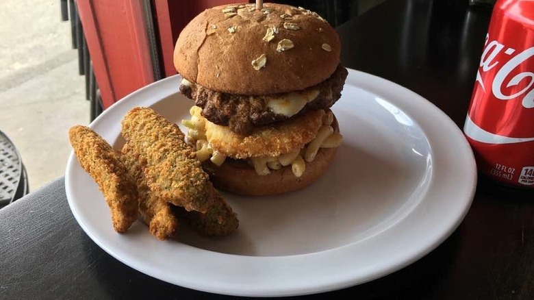 A tall burger from Bob's Atomic Burgers sits on a white plate near a window