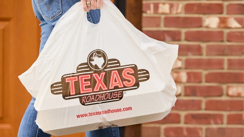Someone carries takeout in a Texas Roadhouse bag.